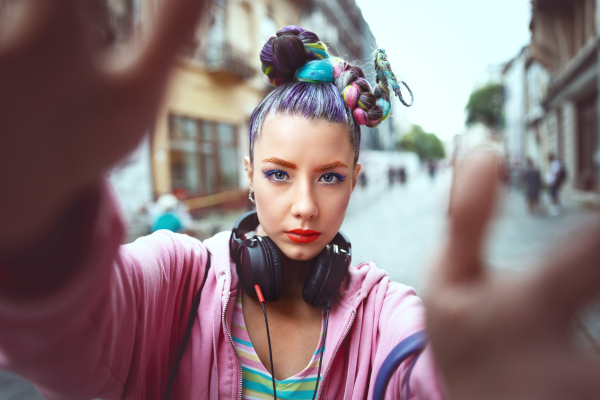 Selfie de uma adolescente com roupas e cabelos coloridos na rua.