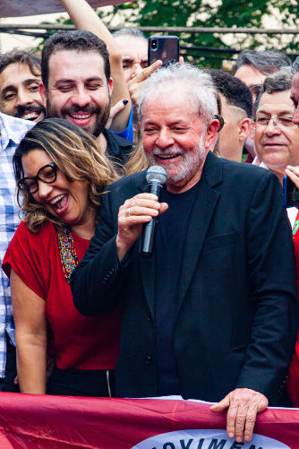 Lula falando ao microfone em comício, após a sua soltura, junto a outras pessoas