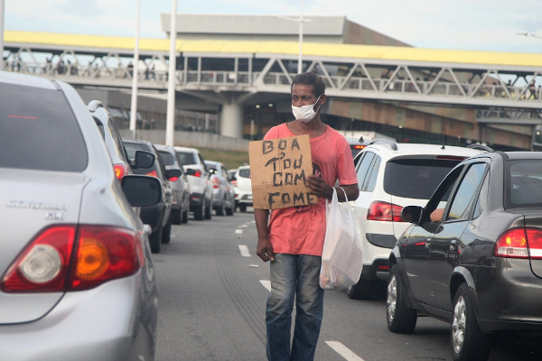 Homem segura placa, em meio ao trânsito, sinalizando estar com fome.