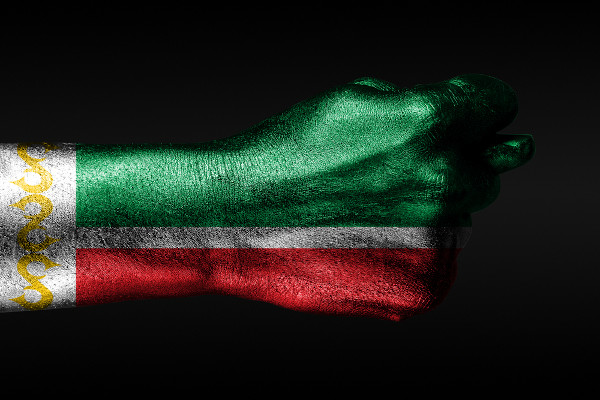 Uma mão com uma bandeira da Chechênia pintada mostra um figo, um sinal de agressão, desacordo, disputa.
