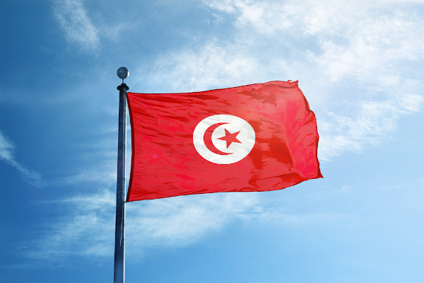Bandeira da Tunísia hasteada e céu azul ao fundo.