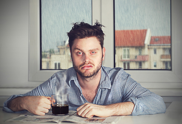 Homem com expressão de cansado segura xícara de café.