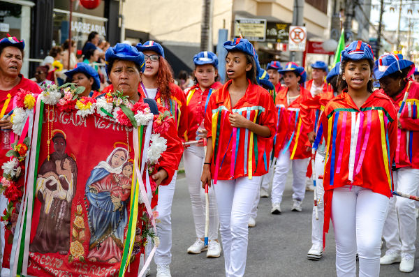 Pessoas com roupas, fitas e bandeiras coloridas em cortejo da congada, em Aparecida, no estado de São Paulo.