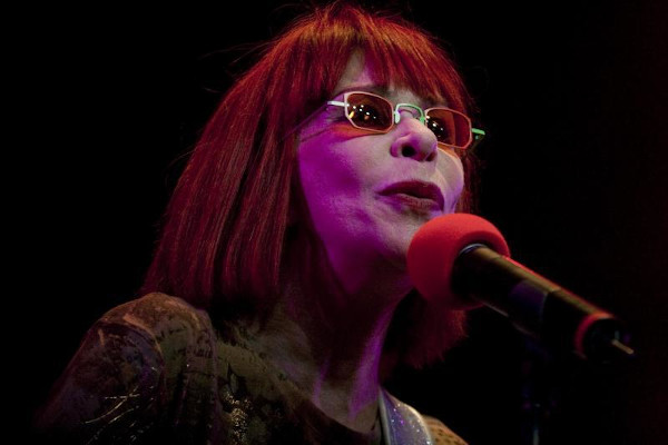 Rita Lee de óculos escuros cantando ao microfone.