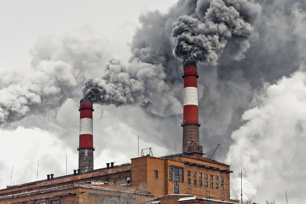 Grande fumaça cinza saindo das chaminés de uma fábrica, uma consequência da industrialização.