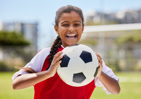 Menina negra sorrindo segurando uma bola de futebol.