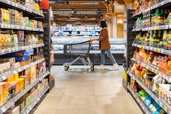 Mulher empurrando um carrinho de compras em um supermercado, representando oferta e procura no livre mercado. 