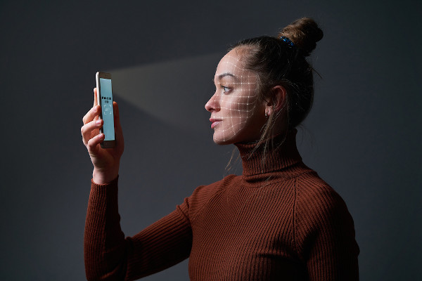 Mulher escaneando o rosto com um celular, utilizando um tipo de inteligência artificial.