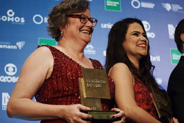 Joice Maria Lamb, ganhadora do Prêmio Educador Nota 10 de 2019. Uma mulher de cabelo curto de vestido vermelho segurando prêmio