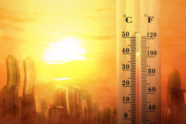 Termômetro registrando altas temperaturas; ao fundo, ambiente urbano sob calor intenso.