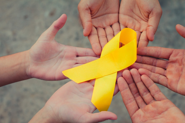 Mãos reunidas e uma fita amarela, símbolo do Dia Mundial de Prevenção ao Suicídio e do Setembro Amarelo, sobre elas. 