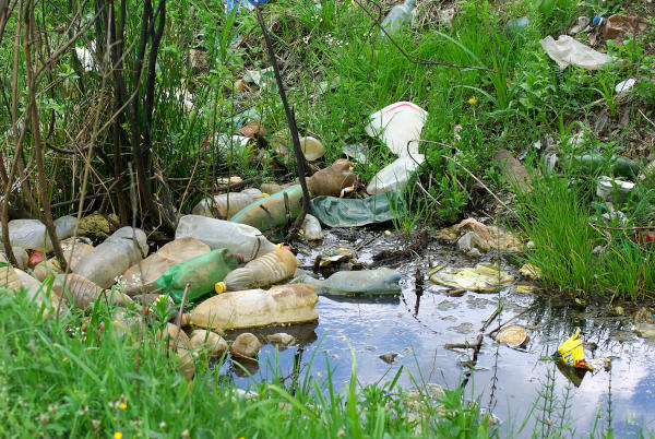 Lixo jogado em um rio e em sua margem, exemplo de poluição hídrica e de poluição dos solos, tipos de degradação ambiental.
