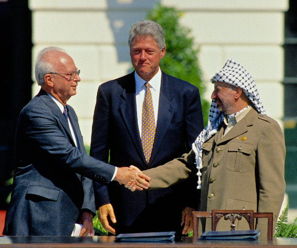 Yitzhak Rabin e Yasser Arafat dão as mãos em 1993. Ao fundo, o presidente Bill Clinton.