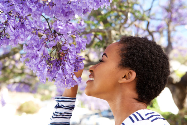 Mulher negra sentindo o cheiro das flores por meio do olfato, um dos cinco sentidos humanos.