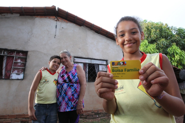 Menina segurando cartão do Bolsa Família, programa que combate a desigualdade social no Brasil, e seus familiares.
