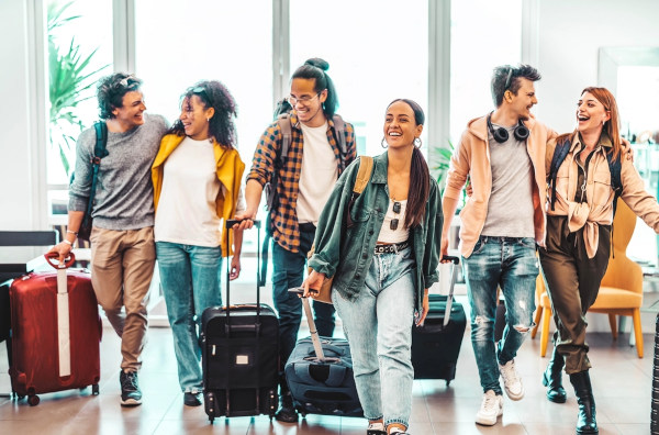 Grupo com seis jovens estudantes segurando malas para viagem de férias.