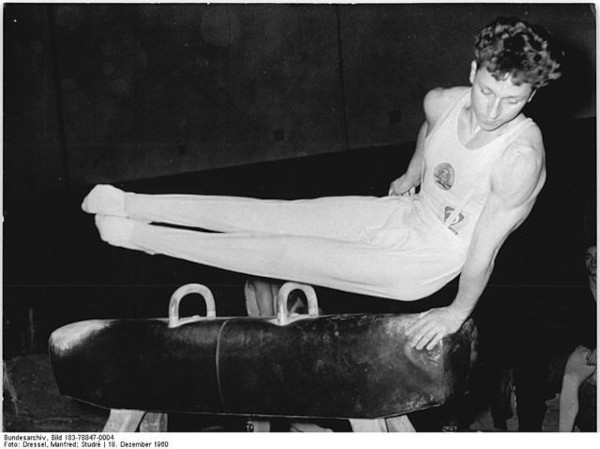 Na foto de 1960, um homem realiza movimento em cavalo com alças, um dos aparelhos da ginástica artística.[2]