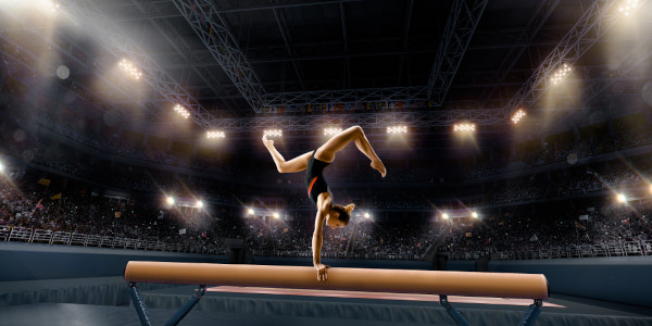 Atleta de ginástica artística fazendo posição com pernas flexionadas enquanto mantém uma parada de mão na trave.