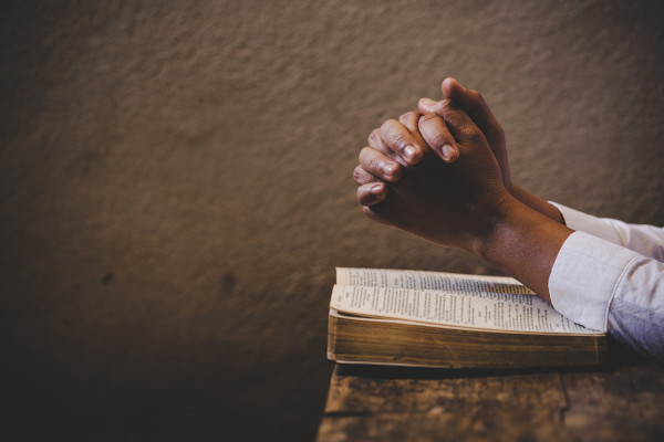 Mãos em posição de oração em cima de bíblia