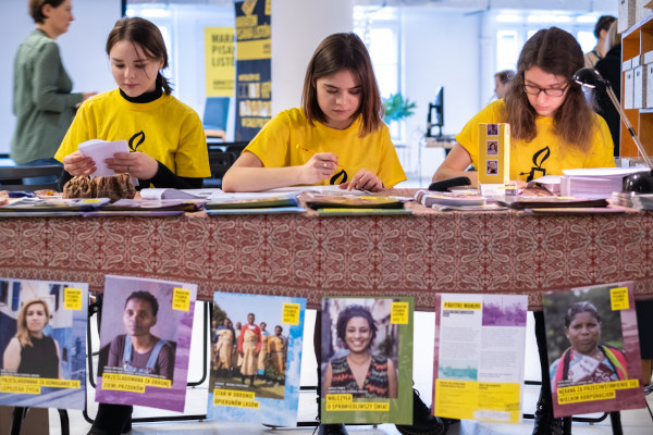 Voluntárias da Anistia Internacional escrevendo sobre mesa com fotos de mulheres.