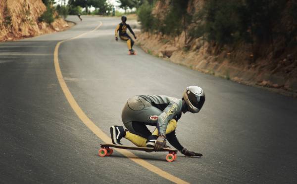 Atletas de skate downhill descendo ladeira em estrada.