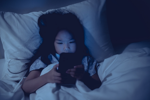 Criança mexendo no celular antes de dormir, uma das causas da insônia, que pode ser reduzida com suplementação de melatonina.