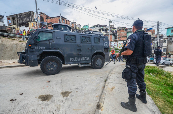 Carro blindado e policial armado em favela, em texto sobre necropolítica.