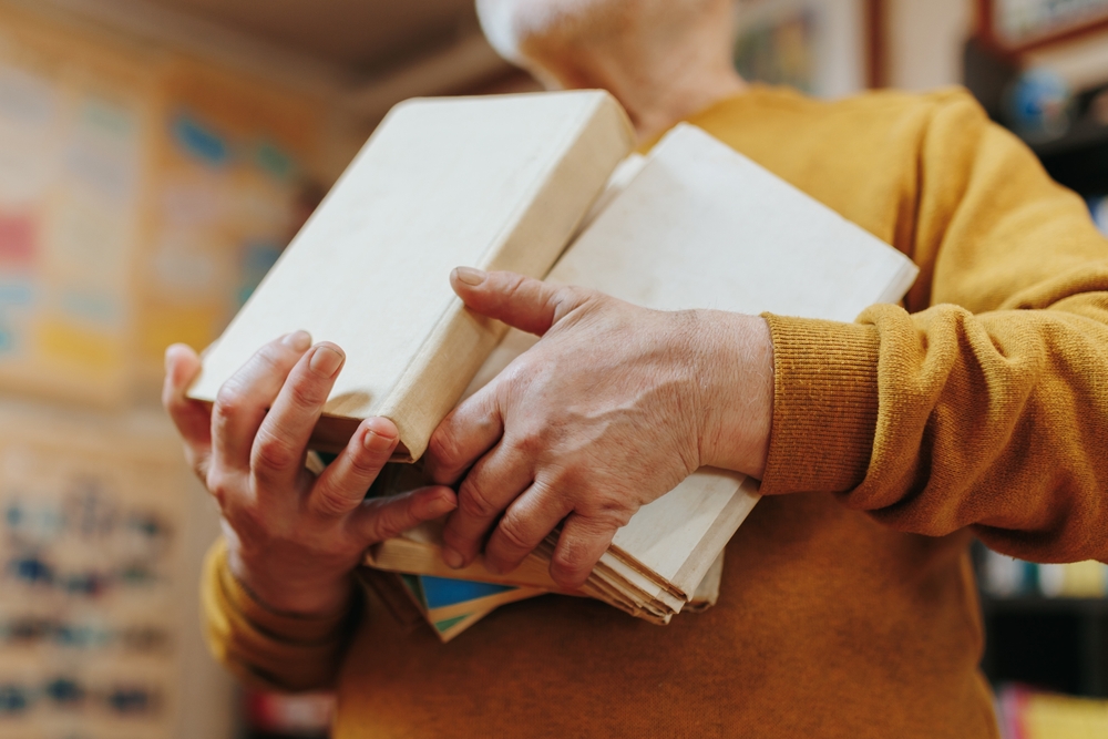 Mãos de uma pessoa mais velha seguram livros em referência às mães na universidade.