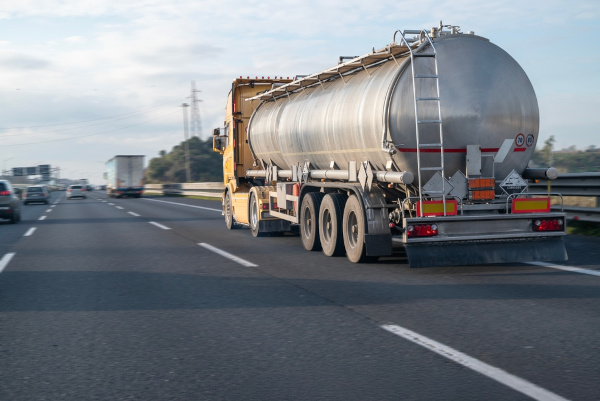 Caminhão-pipa à base de aço inox transportando material corrosivo em via de trânsito rápido.