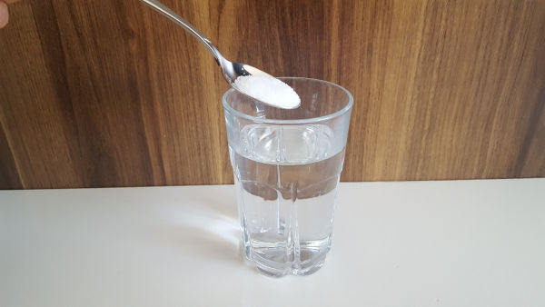 Colher de sal sendo colocada em copo com água, exemplo de solução líquida formada por soluto e solvente.