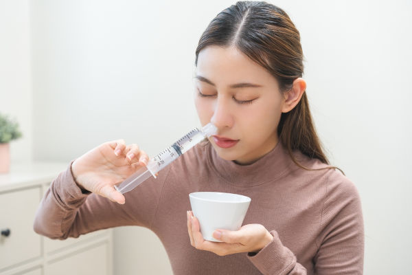 Mulher usando seringa para lavar nariz com soro fisiológico, solução formada por soluto e solvente.