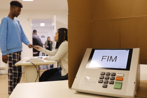 Urna eletrônica e pessoa votando ao lado.