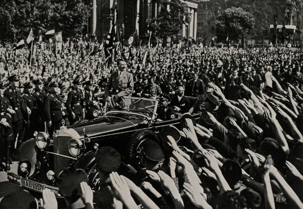 Adolf Hitler desfilando em veículo, cercado e reverenciado por uma multidão durante sua ditadura.