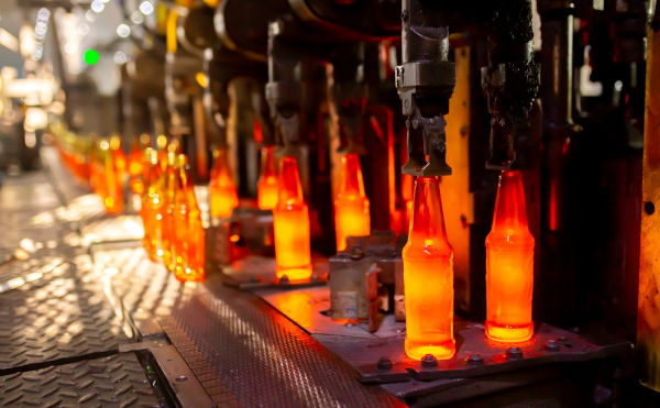 Garrafas de vidro sendo produzidas por fundição em uma fábrica.