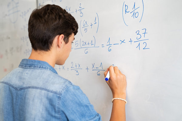 Jovem branco resolvendo cálculo de Matemática em quadro