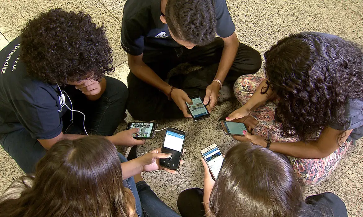 Crian&ccedil;as sentadas em c&iacute;rculo com celulares nas m&atilde;os 