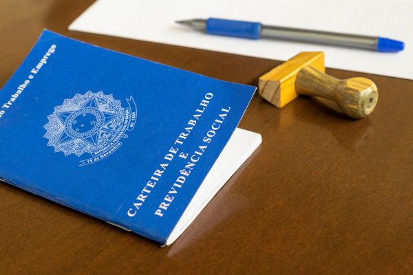 Carteira de trabalho e carimbo sobre uma mesa, em alusão ao mercado de trabalho no Brasil.