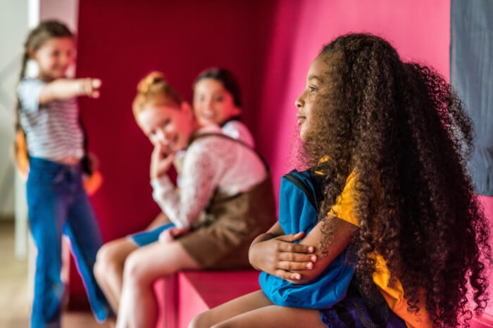 Crianças brancas rindo do cabelo de uma criança negra, para representar o racismo presenta nas escolas.