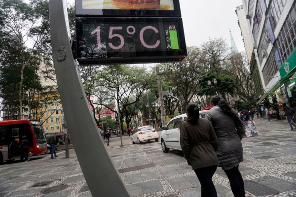 Pessoas caminhando na rua, ao lado de um termômetro marcando 15 °C durante solstício de inverno.