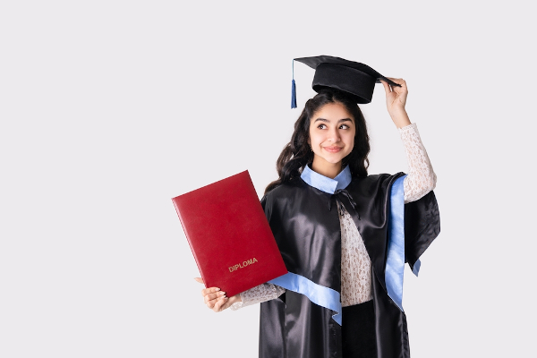 Mulher usando beca e segurando capelo e livro com a palavra diploma, que pode ser de bacharelado, licenciatura ou tecnólogo.