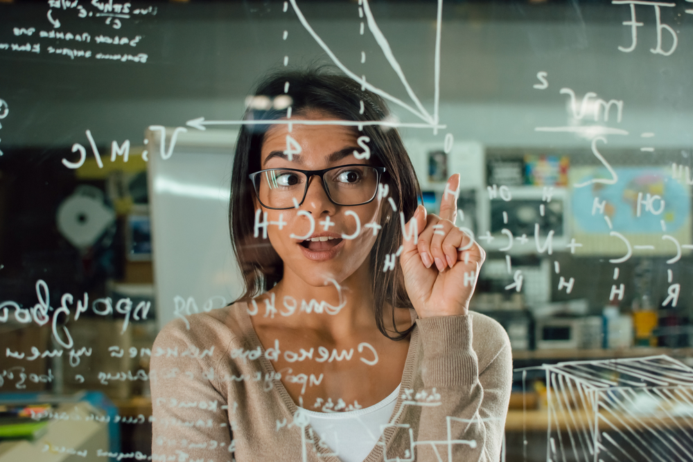 Mulher sorrindo atrás de um quadro transparente com várias contas matemáticas
